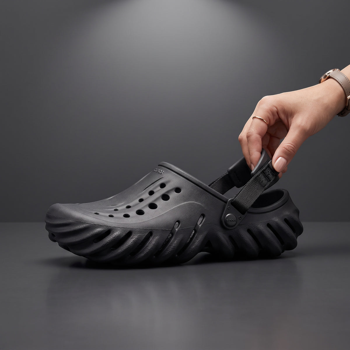 Sabot Echo Clog noir LAS ROSAS en mousse sculptée avec bride ajustable, tenu à la main sur fond gris studio.